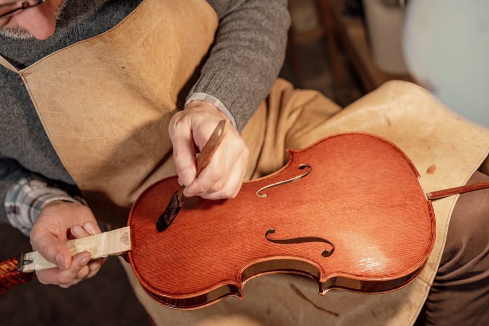 Geigenbauer in Lederschürze lackiert die Decke einer Violine.